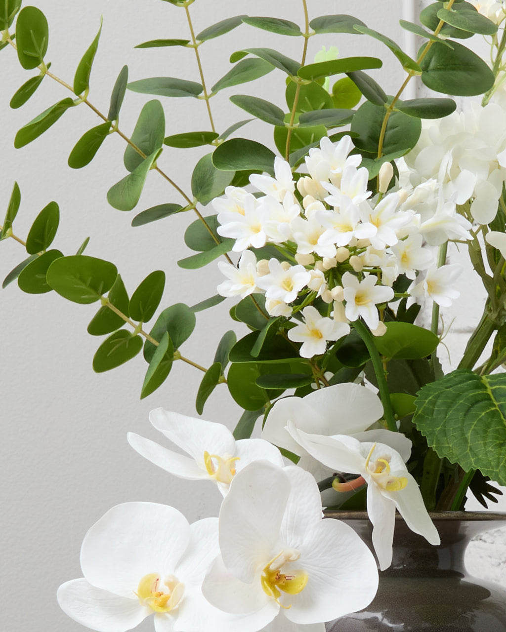 Närbild av Ivory Grace med konstgjorda vita orkidéer med gula mittpartier, vit agapanthus och gröna eukalyptusblad.