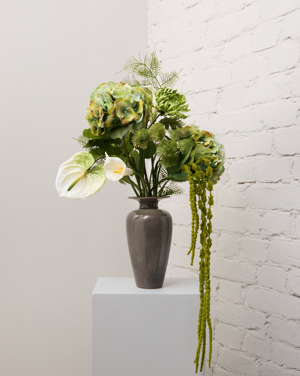 Secret Garden – konstgjord bukett med gröna hortensior, vitgrön anthurium, vit kalla och hängande grön amarant i grå vas.