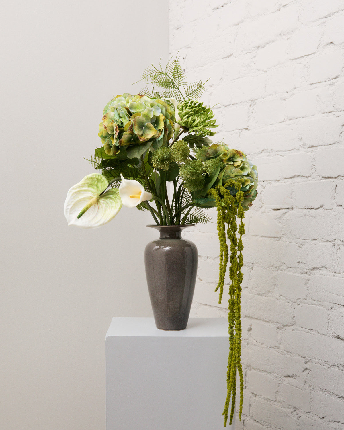 Secret Garden – konstgjord bukett med gröna hortensior, vitgrön anthurium, vit kalla och hängande grön amarant i grå vas.