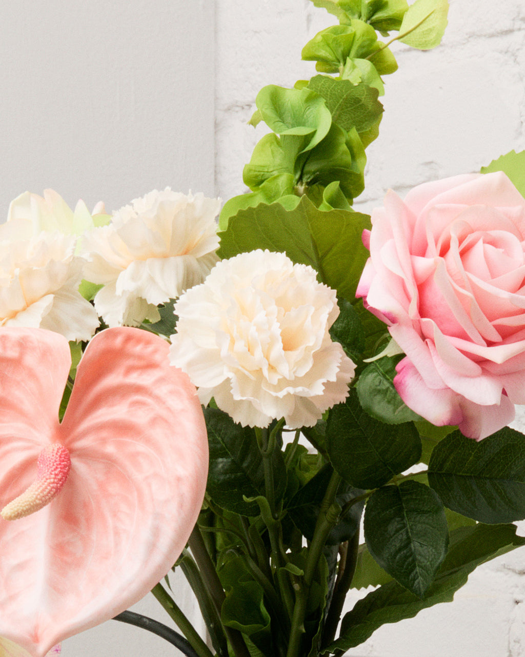 Närbild av Blush Romance med konstgjord ljusrosa ros, rosa hjärtformad anthurium, champagnefärgade nejlikor och grön musselklocka.