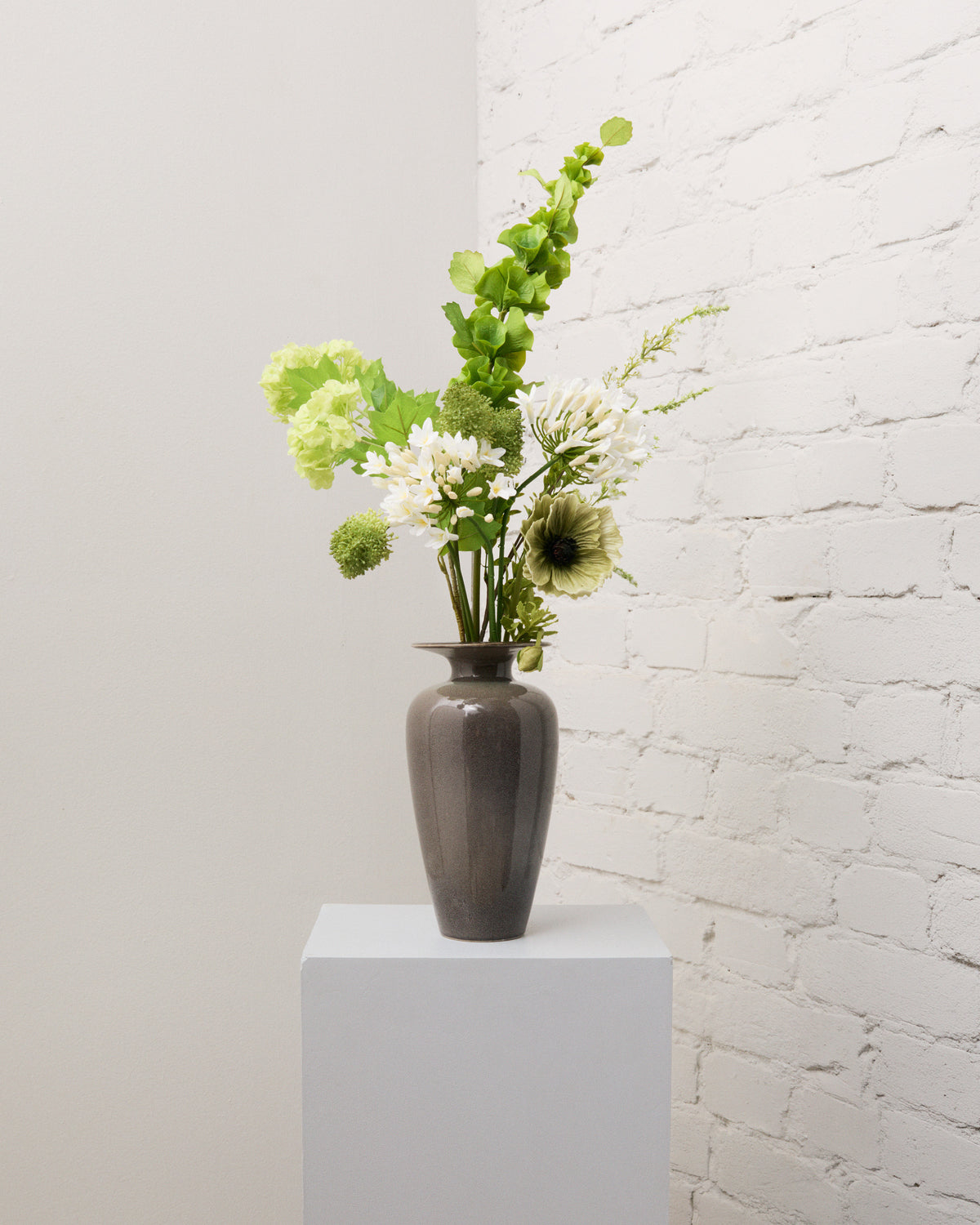 Verdant Whisper – konstgjord bukett i grönt och vitt med agapanthus, grön vallmo, ljusgrön snöbollshortensia och hög musselklocka i grå vas.