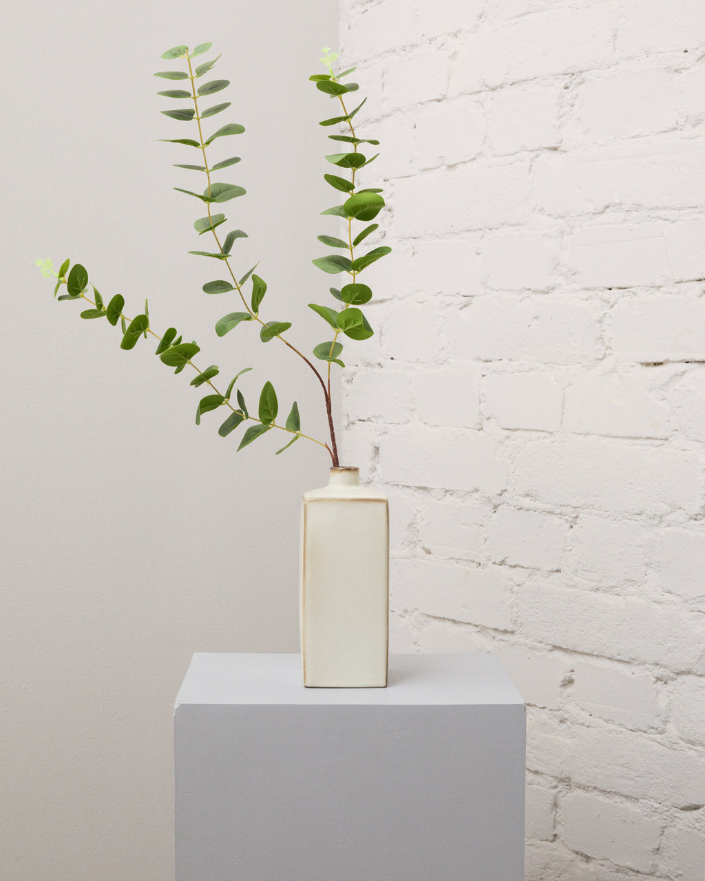 Konstgjord eukalyptus med rundade gröna blad och långa, förgrenade stjälkar i en smal, krämvit vas.