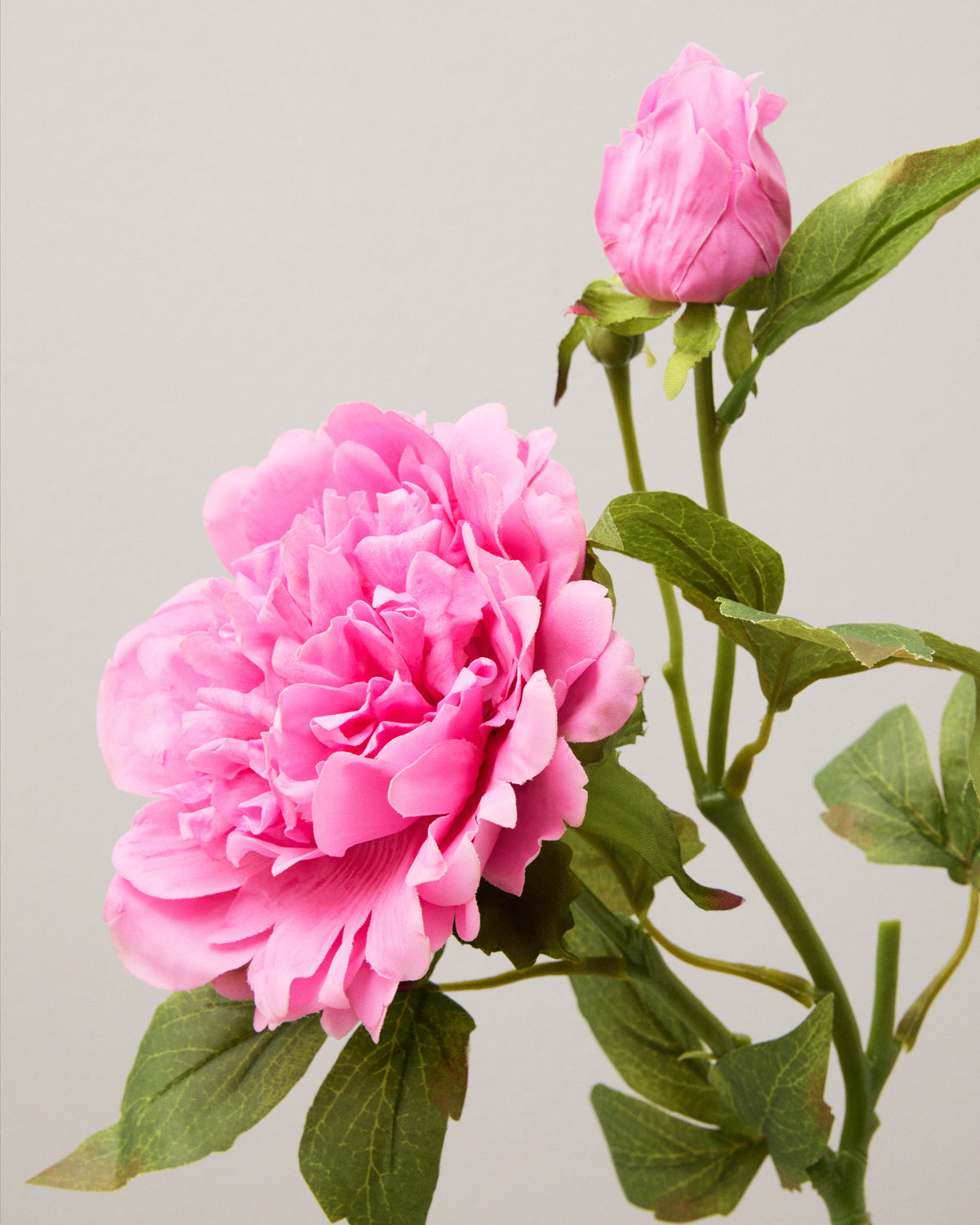 Närbild av konstgjord pion med mörkrosa, vågiga kronblad i täta lager, en rosa knopp och gröna blad.