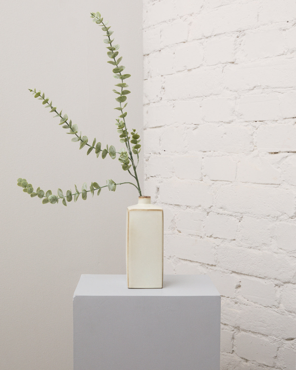 Konstgjord eukalyptus med silvergröna, rundade blad och långa, förgrenade stjälkar i en smal, krämvit vas.