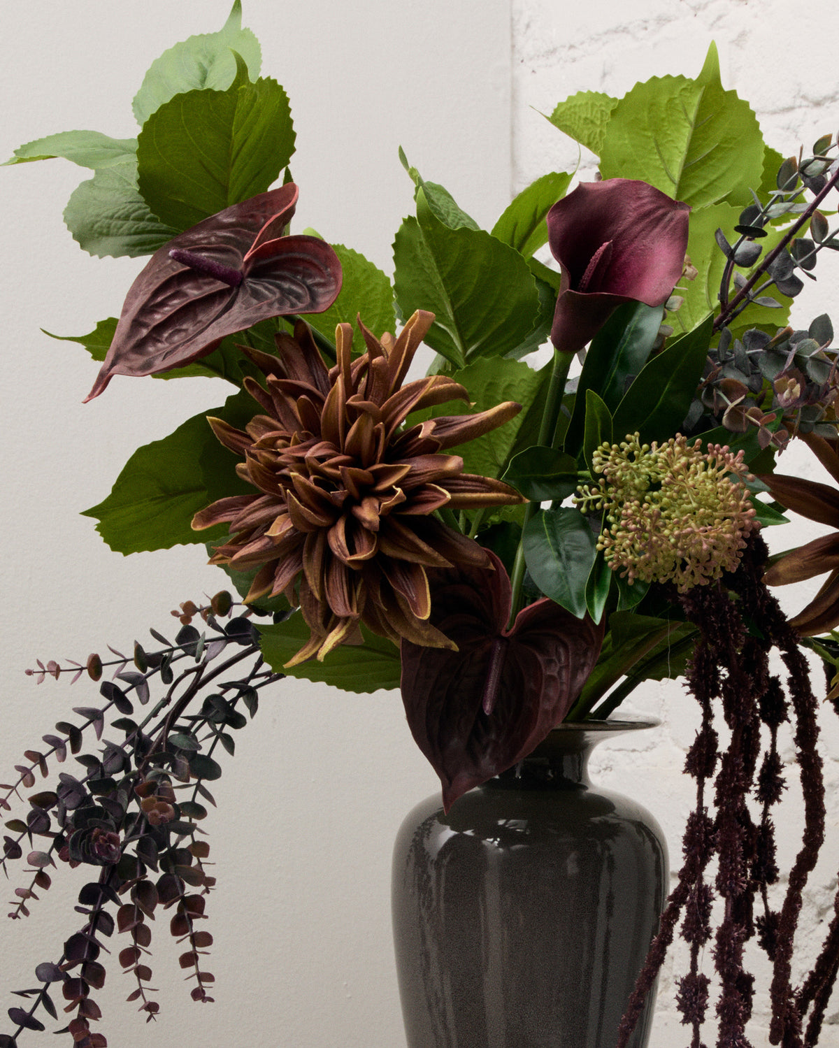 Närbild av Midnight Bloom med konstgjord kastanjebrun dahlia, vinröd anthurium och kalla omgivna av gröna hortensiablad.